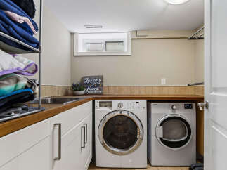 This laundry room features a stacked washer and dryer set, ample cabinet storage, and a utility sink for added convenience.
