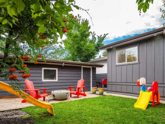 Enjoy outdoor living in this charming backyard featuring a spacious wooden deck, a modern fire pit, and vibrant red Adirondack chairs perfect for relaxation.