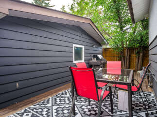 Enjoy outdoor living with this charming patio featuring a glass-top dining table and vibrant red chairs, perfect for al fresco meals.