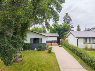 Charming bungalow with a modern dark gray and white exterior, featuring a welcoming wooden deck and a spacious driveway.
