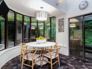 Enjoy your morning coffee in this bright and airy breakfast nook, surrounded by lush greenery through expansive windows.