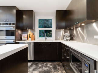 Experience culinary excellence in this modern kitchen, featuring sleek dark wood cabinetry and a stunning stainless steel backsplash.