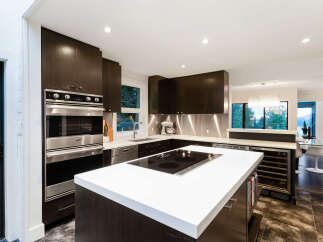 Experience modern luxury in this stunning kitchen, featuring sleek dark wood cabinetry and a spacious white quartz island with a built-in cooktop.