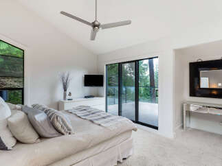 Experience luxury living in this stunning bedroom featuring a vaulted ceiling with a modern ceiling fan and a unique triangular window offering breathtaking forest views.