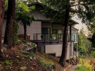 Nestled amidst lush greenery, this modern home offers a serene retreat with its expansive deck and large windows, perfect for enjoying the surrounding natural beauty.