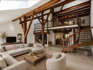 Experience rustic charm and modern comfort in this stunning living space, featuring exposed wooden beams, a grand fireplace, and a spacious sectional sofa.