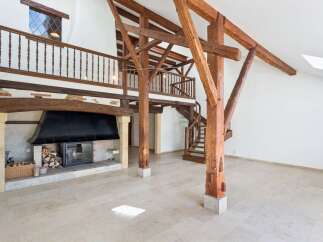 Experience rustic charm in this spacious living area featuring exposed wooden beams and a grand stone fireplace.