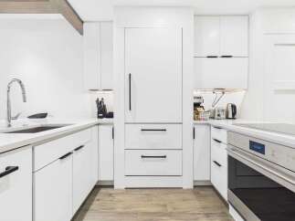 Experience modern living in this stunning white kitchen, featuring sleek cabinetry and a built-in refrigerator.