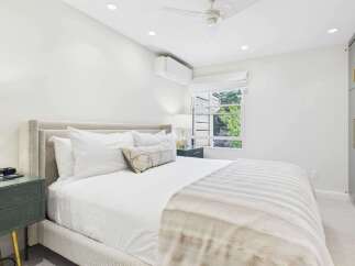 Experience ultimate comfort in this beautifully appointed bedroom, featuring a plush king-sized bed with crisp white linens and a decorative lumbar pillow.