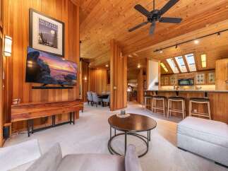 Experience rustic charm in this stunning living space featuring warm wood paneling throughout and a vaulted ceiling with a ceiling fan.