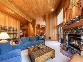 Experience rustic charm in this spacious living room, featuring a stunning floor-to-ceiling stone fireplace and warm, wood-paneled walls and ceiling.