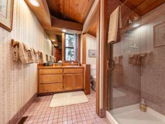 This charming bathroom features a wooden vanity with ample storage and a large mirror, complemented by a tiled shower with a glass door.