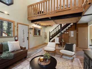 Experience rustic charm in this inviting living space featuring a cozy leather sofa and a unique lofted bedroom accessible by a wooden staircase.
