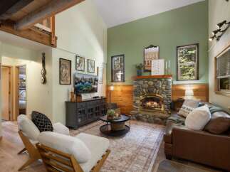 Cozy up by the stone fireplace in this inviting living room, featuring a comfortable leather sofa and two accent chairs perfect for relaxation.