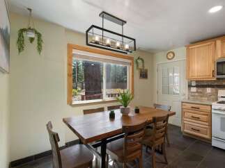 Enjoy meals with a view in this charming dining area, featuring a rustic wooden table and chairs bathed in natural light from a large window overlooking a serene forest.