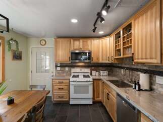 This charming kitchen features light wood cabinetry, a white gas range, and a stainless steel microwave.