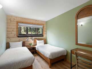 Experience rustic charm and natural beauty in this inviting bedroom featuring two comfortable twin beds and a large window overlooking a serene forest.