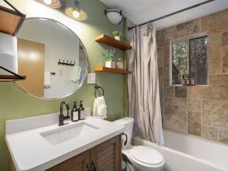 This charming bathroom features a modern vanity with a white countertop and a rustic wood cabinet, complemented by a round mirror and stylish fixtures.