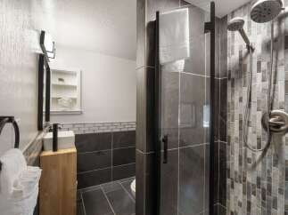 Experience modern luxury in this stunning bathroom, featuring a sleek glass-enclosed shower with a dual showerhead and intricate mosaic tilework.