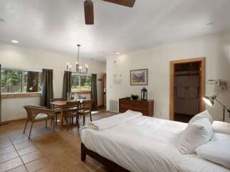Experience cozy living in this charming studio apartment, featuring a comfortable bed, a dedicated dining area, and large windows offering serene forest views.