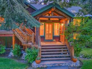 Experience rustic charm with this beautiful log cabin home, featuring a welcoming wooden porch and staircase leading to the entrance.