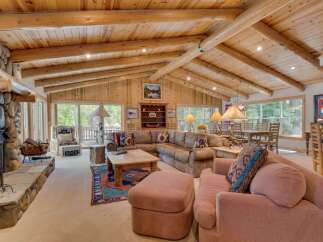 Experience rustic charm in this spacious log cabin living room, featuring a grand stone fireplace and exposed wooden beams that create a warm, inviting atmosphere.