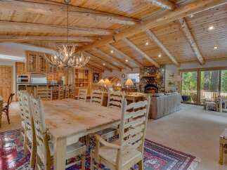 Experience rustic elegance in this spacious log cabin dining and living area, featuring a grand antler chandelier and a magnificent stone fireplace.
