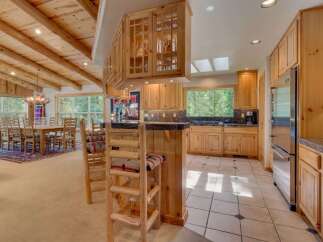 Experience rustic charm in this spacious kitchen and dining area, featuring a vaulted wood-beamed ceiling and a grand antler chandelier.