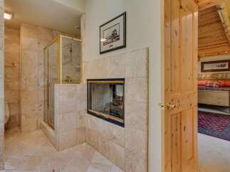 Experience luxury and comfort in this master suite, featuring a spacious tiled shower with gold fixtures and a cozy gas fireplace.