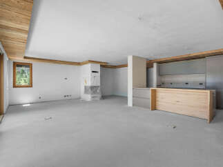 This spacious, unfinished living area features a modern kitchen island with a light wood finish, complemented by sleek grey cabinetry and stainless steel appliances.