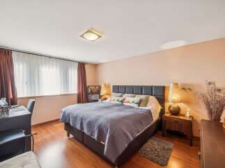 This inviting bedroom features a spacious bed with a dark upholstered headboard, complemented by a plush blue quilted comforter and decorative pillows.