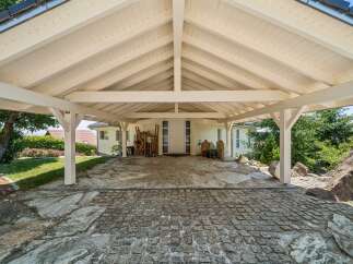 This property features a charming white carport with a sloped wooden ceiling, supported by sturdy white pillars.