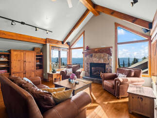 Experience breathtaking mountain views from this stunning living room, featuring a cozy stone fireplace and comfortable leather seating.