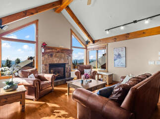 Experience breathtaking mountain views from this stunning living room, featuring a grand stone fireplace and expansive triangular windows that flood the space with natural light.