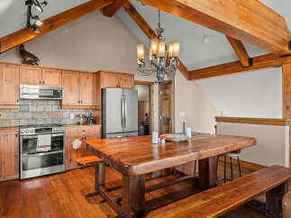 Experience rustic charm in this spacious kitchen and dining area, featuring warm wood cabinetry, a stainless steel appliance suite, and a grand wooden dining table perfect for gatherings.
