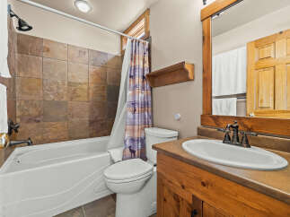 This rustic bathroom features a deep soaking tub with slate tile surround and a charming woodland-themed shower curtain.