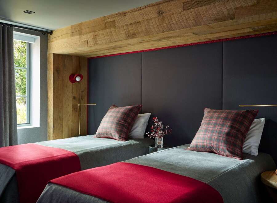 Experience rustic charm and modern comfort in this inviting bedroom, featuring two twin beds adorned with cozy plaid pillows and vibrant red throws.