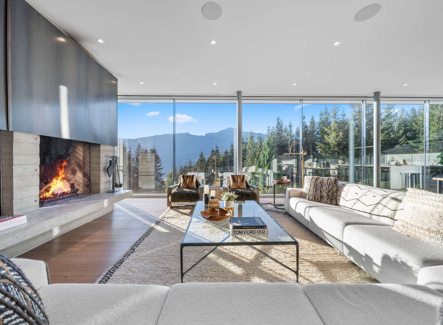 Experience breathtaking mountain views from this modern living room, featuring a striking concrete fireplace and expansive floor-to-ceiling windows.