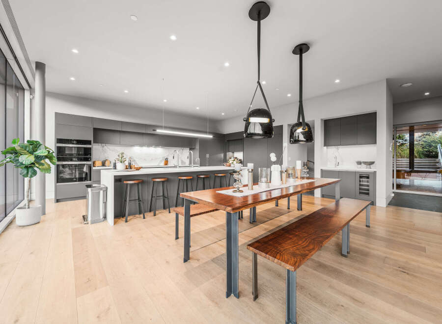Experience modern luxury in this stunning open-concept kitchen and dining area, featuring sleek grey cabinetry, a large island with bar seating, and a beautiful live-edge dining table.