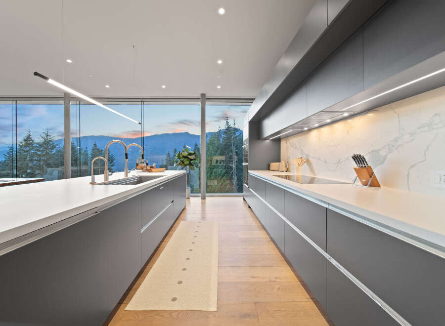 Experience modern luxury in this stunning kitchen featuring sleek grey cabinetry and a breathtaking panoramic view of the mountains and forest.