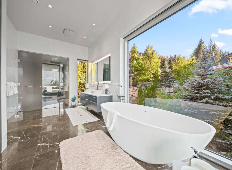Experience luxury in this modern bathroom featuring a stunning freestanding bathtub with a panoramic view of the lush, green outdoors.