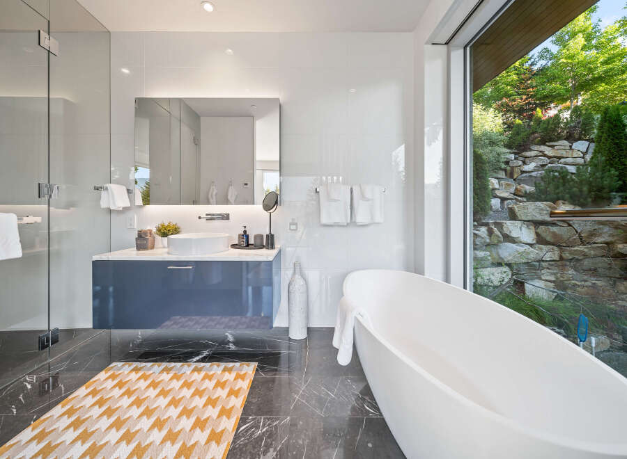Experience luxury in this modern bathroom featuring a freestanding soaking tub with a stunning view of a lush, rocky landscape.