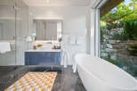 Experience luxury in this modern bathroom featuring a freestanding soaking tub with a stunning view of a lush, rocky landscape.