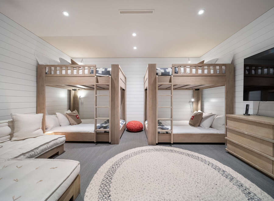 This spacious bedroom is designed for comfort and fun, featuring two sets of twin bunk beds with natural wood finishes and crisp white linens.