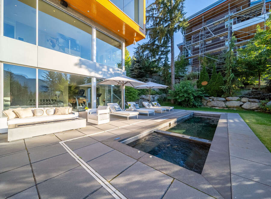Experience luxury outdoor living with this modern patio featuring a sleek fire pit sofa, comfortable lounge chairs, and a refreshing pool and spa.