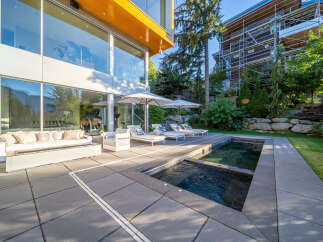 Experience luxury outdoor living with this modern patio featuring a sleek fire pit sofa, comfortable lounge chairs, and a refreshing pool and spa.
