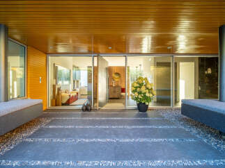 Step into modern luxury with this stunning entryway featuring sleek wooden ceilings and a vibrant orange accent wall.