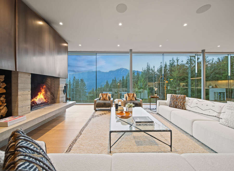 Experience luxury living in this stunning modern living room, featuring a dramatic concrete fireplace with a stacked wood accent and a sleek metal surround.