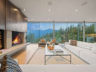 Experience luxury living in this stunning modern living room, featuring a dramatic concrete fireplace with a stacked wood accent and a sleek metal surround.