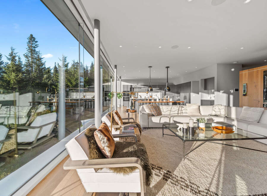 Experience modern luxury in this stunning open-concept living space, featuring floor-to-ceiling windows that bathe the room in natural light and offer breathtaking views of the surrounding forest.